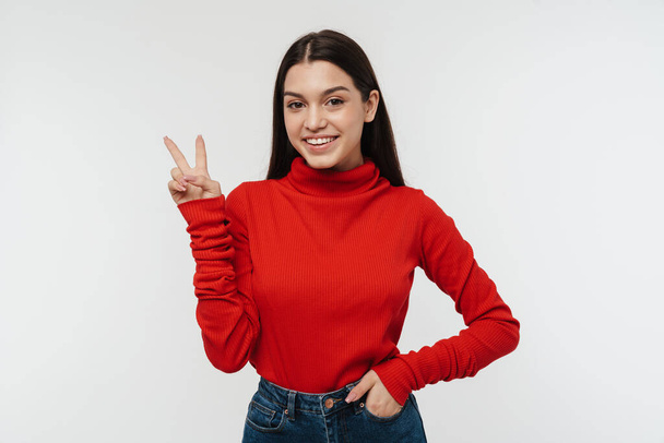 Portrait of a pretty cheerful young brunette woman wearing casual clothing isolated over white background, peace gesture - Photo, Image