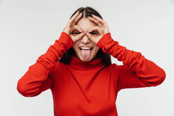 Photo of amusing young woman making fun with fingers and sticking out her tongue isolated over white wall - Foto, Bild