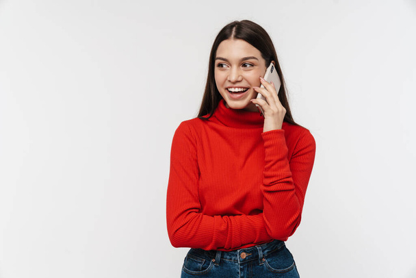 Photo of happy caucasian young woman smiling while talking on mobile phone isolated over white wall - Foto, afbeelding