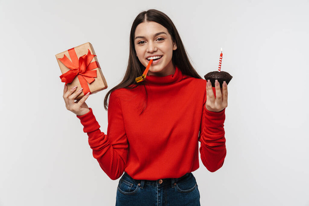 Photo of happy caucasian woman with party horn holding gift box and cake isolated over white wall - Foto, Bild
