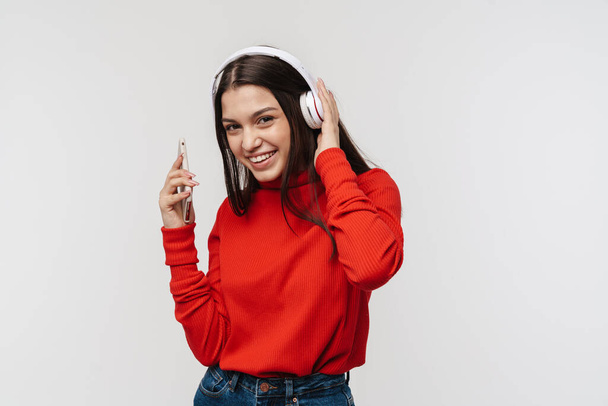 Photo of happy caucasian woman smiling while using cellphone and headphones isolated over white wall - Фото, изображение