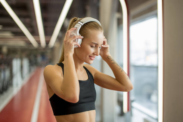 Sport and Music. woman hold headphones while working out in gym - Photo, Image