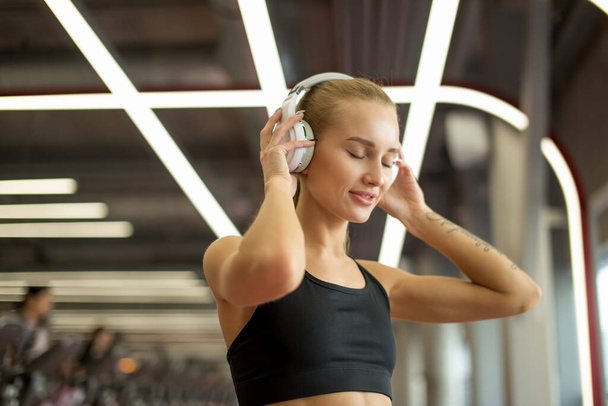 Sport and Music. woman hold headphones while working out in gym - Fotoğraf, Görsel