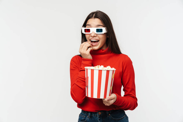Photo of pleased brunette woman wearing 3D glasses holding popcorn bucket isolated over white background - Foto, Imagen