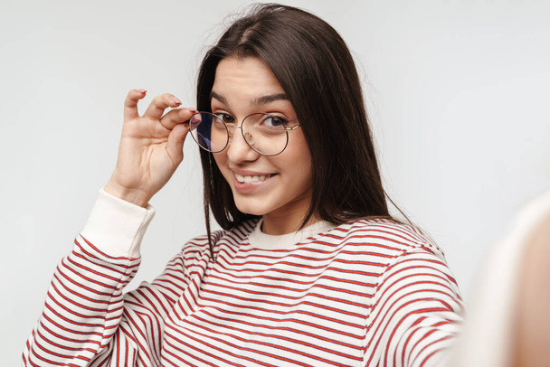 Photo of happy brunette young woman wearing eyeglasses smiling at camera isolated over white background - Фото, зображення