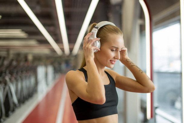 Sport and Music. woman hold headphones while working out in gym - Фото, зображення