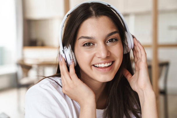 Photo of smiling beautiful woman using wireless headphone while sitting in bed after sleep - Foto, Bild