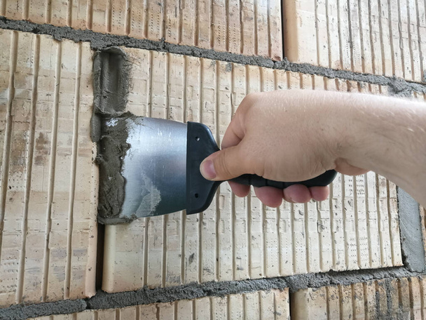 Construction worker hand holding taping knife tool with glues at construction site - Photo, Image