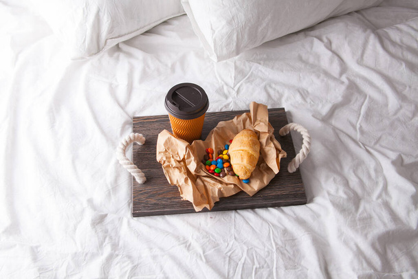 Desayuno romántico con rama de flores en la cama en bandeja de madera con hojuelas de maíz, frutas, leche, huevos y café. Luz de ventana, espacio de copia - Foto, imagen