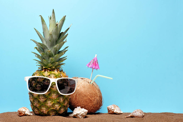 Piña con gafas de sol en arena con bebida de coco sobre un fondo azul. concepto de playa de verano
. - Foto, imagen