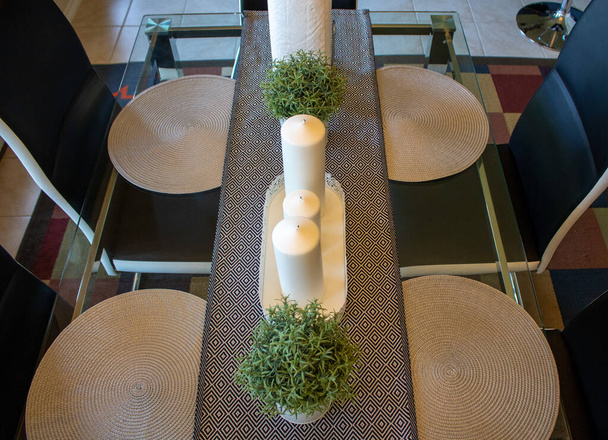 Mesa de comedor decorada con velas blancas establece plantas en maceta en un corredor gris
 - Foto, imagen