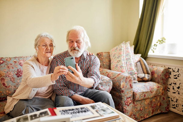 Happy senior couple with smartphone taking selfie at home, old age, technology. - Φωτογραφία, εικόνα