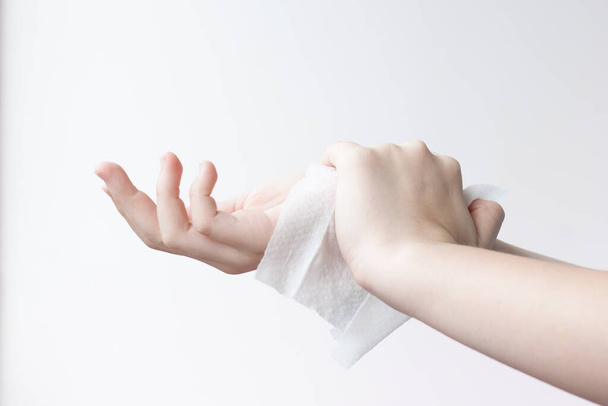 One hand wipes the other hand with a damp antibacterial cloth on a light background - 写真・画像