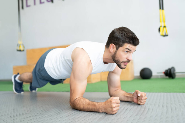 Determined Hispanic young man doing plank exercise at health club - Photo, Image