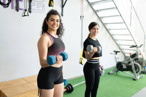 Magabiztos spanyol fiatal nők, akik súlyzókkal gyakorolnak a fitneszklubban. - Fotó, kép