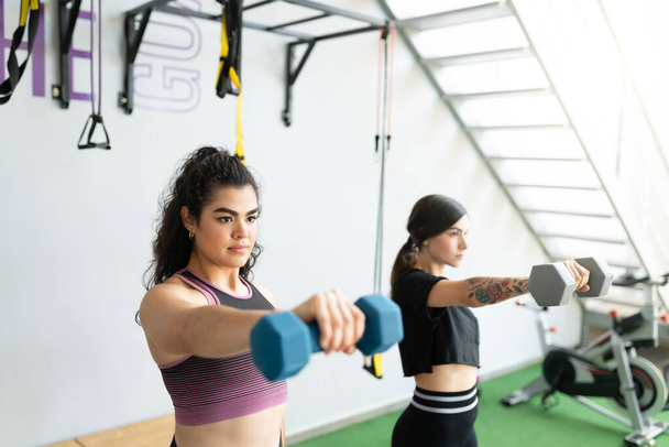 Привлекательная спортивная форма для молодых женщин, тренирующихся с гантелями в тренажерном зале - Фото, изображение