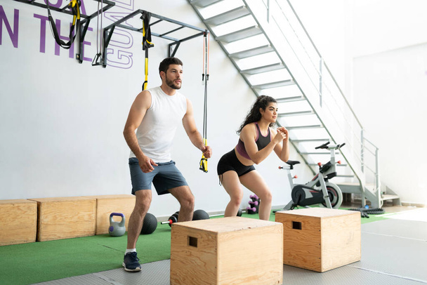Визначення латинського юнака і жінки, які роблять стрибки в коробках під час крос-тренінгу в медичному клубі - Фото, зображення