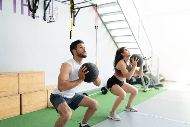 Athletic Latin young man and woman exercising with wallballs at fitness club - Photo, Image