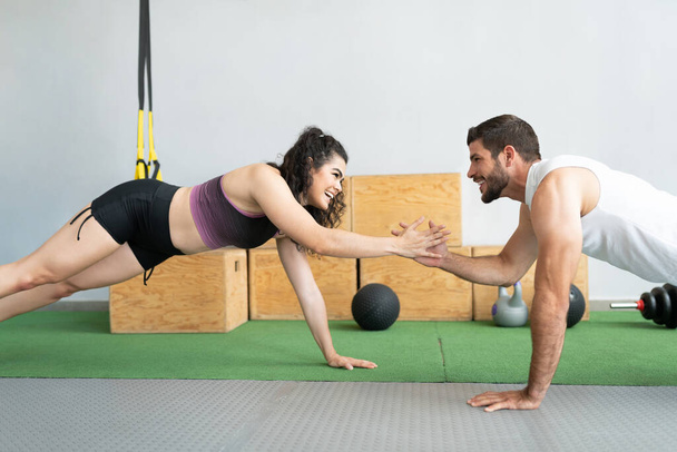 Latin young man and woman clapping hands while doing push-ups together at health club - Photo, Image