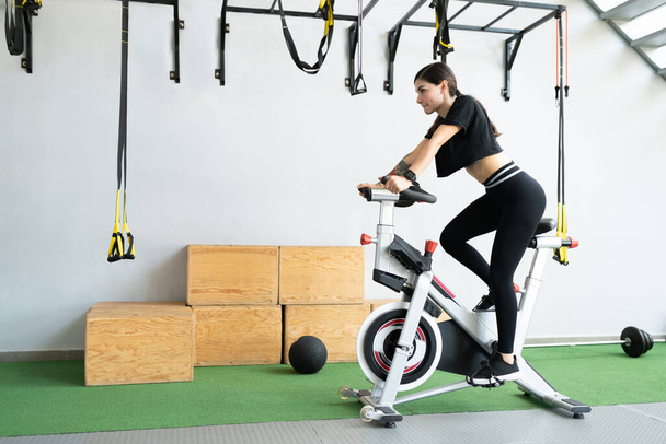 Confident fit young woman cycling on exercise bike at cross-training gym - Fotoğraf, Görsel