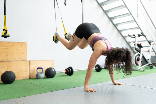 Jeune femme latine sportive faisant de l'exercice pendant la formation de suspension à la salle de gym - Photo, image