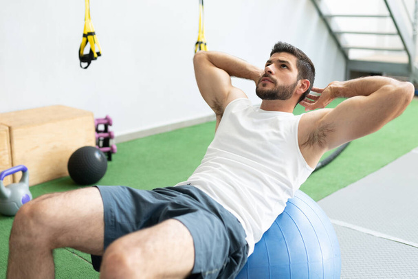 Handsome young man doing workout with fitness ball at health club - Fotografie, Obrázek