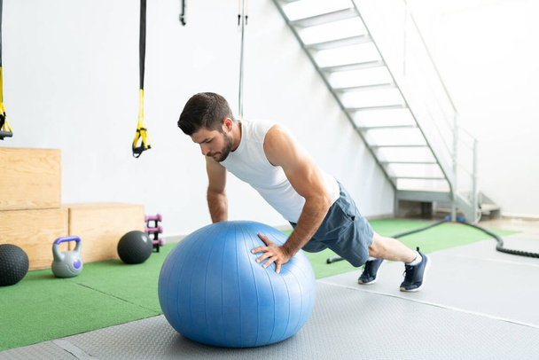 Latin young man doing push-ups on fitness ball during cross-training at gym - Photo, Image