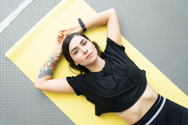 Прямо над кадром спортивная молодая женщина лежит на коврике для упражнений - Фото, изображение