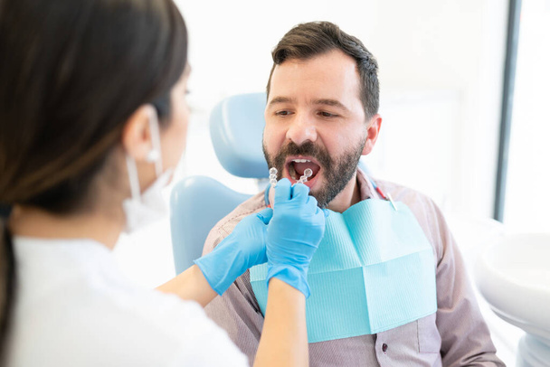 Görünmez diş teli olan kadın ortodontist yetişkin adamı muayene ediyor. - Fotoğraf, Görsel