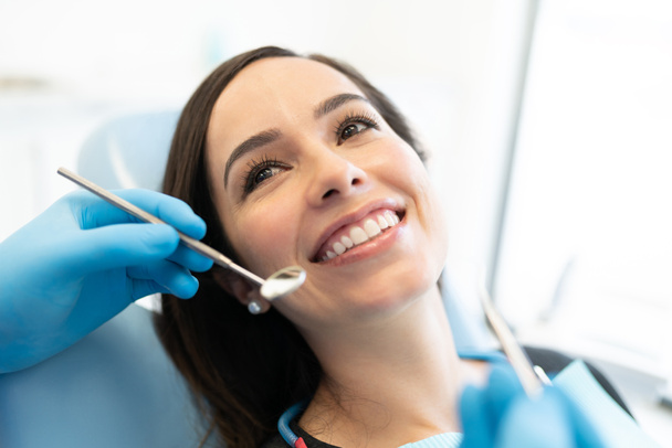 Стоматолог проверяет белую женщину с резчиком и зеркалом в стоматологической клинике - Фото, изображение
