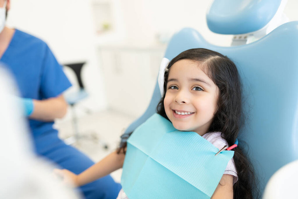 Souriant mignon hispanique fille assise sur la chaise à la clinique dentaire - Photo, image