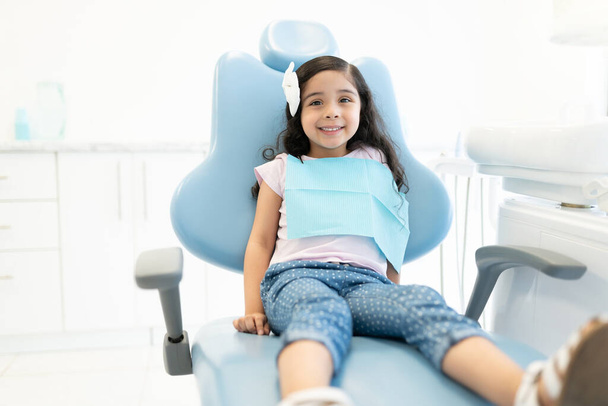 Sorridente carina ragazza ispanica seduta sulla sedia alla clinica dentale - Foto, immagini