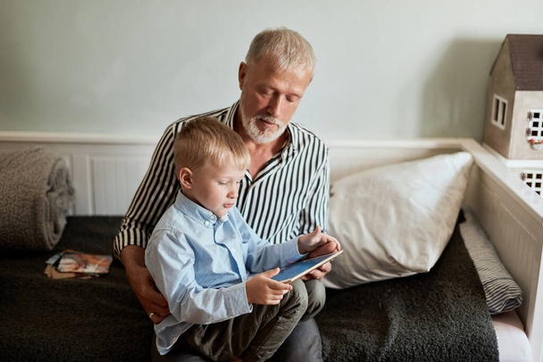 Grandfather and grandson using digital tablet while sitting on couch - Foto, Bild