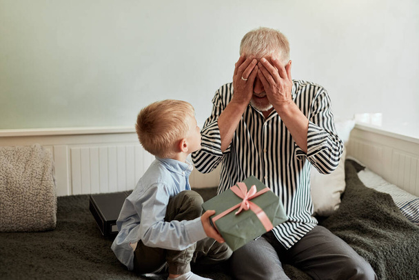 generation. grandfather and grandson with gift box sitting on couch at home - Photo, Image