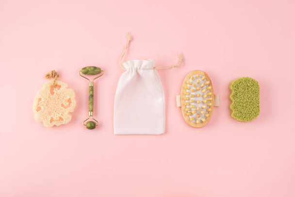 Anti cellulite massager, bamboo sponge, face jade roller, cotton bag, loofah sponge on pastel pink. Set of bathroom accessories. Zero waste concept. - Fotó, kép