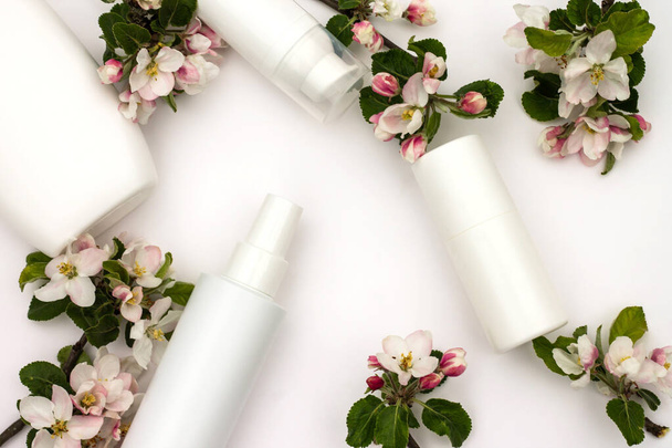 Bílé kosmetické láhve s hruškovými květy na bílém pozadí. Přírodní koncepce organické kosmetiky. - Fotografie, Obrázek