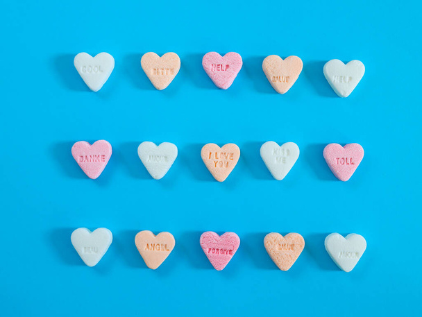 Hartvormige snoepjes in verschillende pasteltinten liggen in het midden in drie rijen op een blauwe papieren achtergrond, bovenaanzicht close-up. - Foto, afbeelding