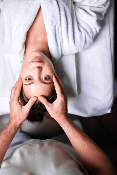 Woman enjoying anti aging facial massage. Upside down photo of relaxing woman - Foto, afbeelding
