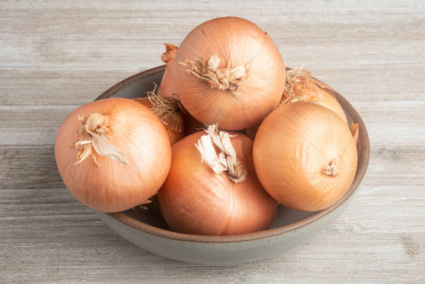 A bunch of authentic southern sweet onions artfully arranged on a ceramic bowl placed on a white painted rustic wood panel board. - Photo, Image