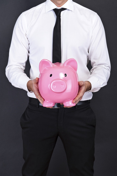 Young man with piggy bank (money box), on dark background - Foto, Bild