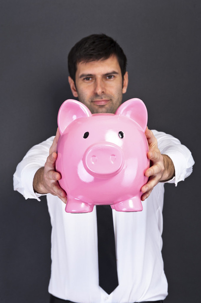 portrait of young man holding a piggy bank against a grunge back - Photo, Image