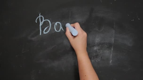 female hand holds blue chalk and writes back to school on black chalk board, start of the school year - Footage, Video