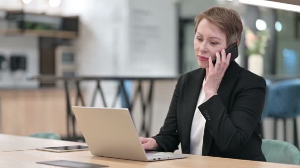 Old Businesswoman with Laptop Talking on Smartphone  - Кадри, відео