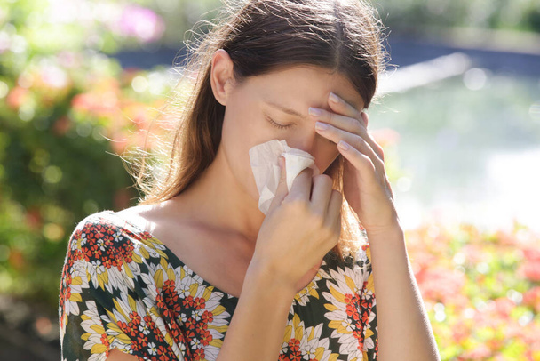 Seasonal allergies. Young girl blowing nose and sneezing in tissue in the park.  - Zdjęcie, obraz