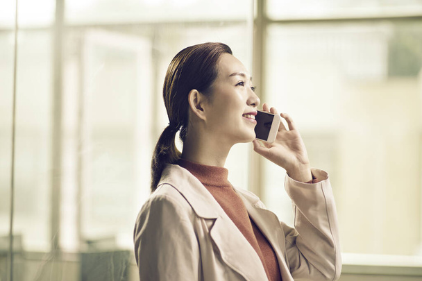 smiling young asian business woman making a call in office using cellphone - 写真・画像