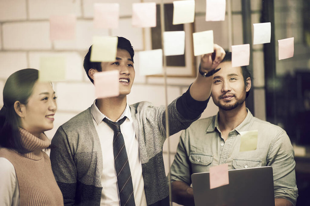 τρεις ασιατικές μικρές επιχειρήσεις επιχειρηματίες νέοι επιχειρηματίες meeing συζήτηση στο γραφείο χρησιμοποιώντας κολλώδεις σημειώσεις - Φωτογραφία, εικόνα