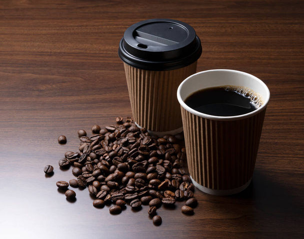 Een papieren kopje koffie en koffiebonen op een houten achtergrond - Foto, afbeelding