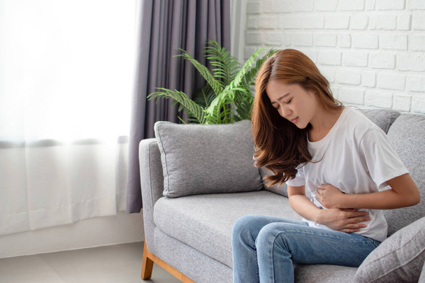 Le donne asiatiche hanno mal di stomaco o mestruazioni. Si sedette sul divano nel soggiorno. - Foto, immagini