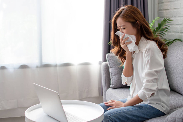 Mulher de negócios asiática está espirrando no sofá. Ela trabalha em um laptop em casa
. - Foto, Imagem