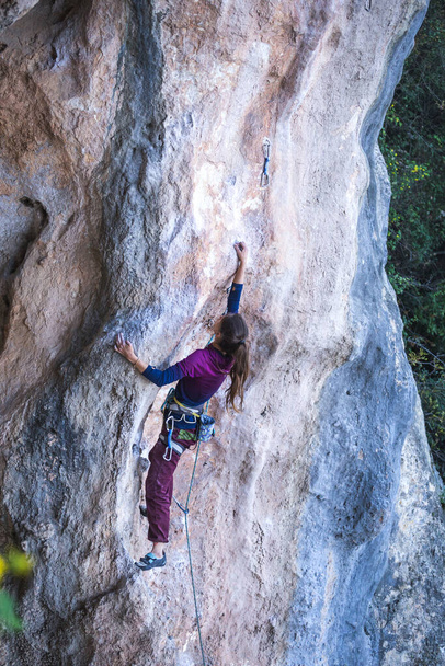 Een meisje beklimt een rots op de achtergrond van het bos, De atleet traint in de natuur, Vrouw overwint moeilijke klimroute, Sterke klimmer, Extreme hobby, Rotsklimmen in Turkije. - Foto, afbeelding